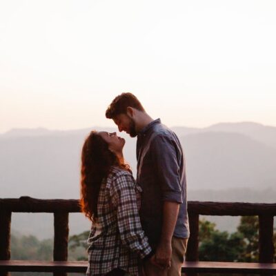 Free Side view of loving young casual couple holding hands and looking at each other while resting on terrace in mountainous valley at sunset Stock Photo